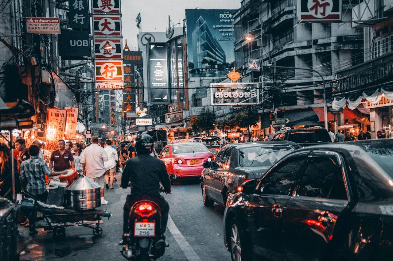 A busy Bangkok street at dusk with taxis, motorbikes and glowing neon signs amid heavy traffic - the kind of after-dark energy a short walk from a central Sukhumvit base